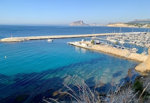 A marina with boats docked, clear blue water, and a rocky shoreline.