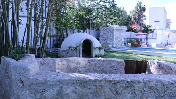 A stone structure with an arched entrance, surrounded by bamboo and greenery, with a pool and umbrellas in the background. - Charming 5-Bed Villa in Cancún (Cancún)