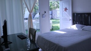 A bedroom with a bed, a desk, and a chair. There is a window with curtains, a door with a star decoration, and a view of a garden. - Charming 5-Bed Villa in Cancún (Cancún)