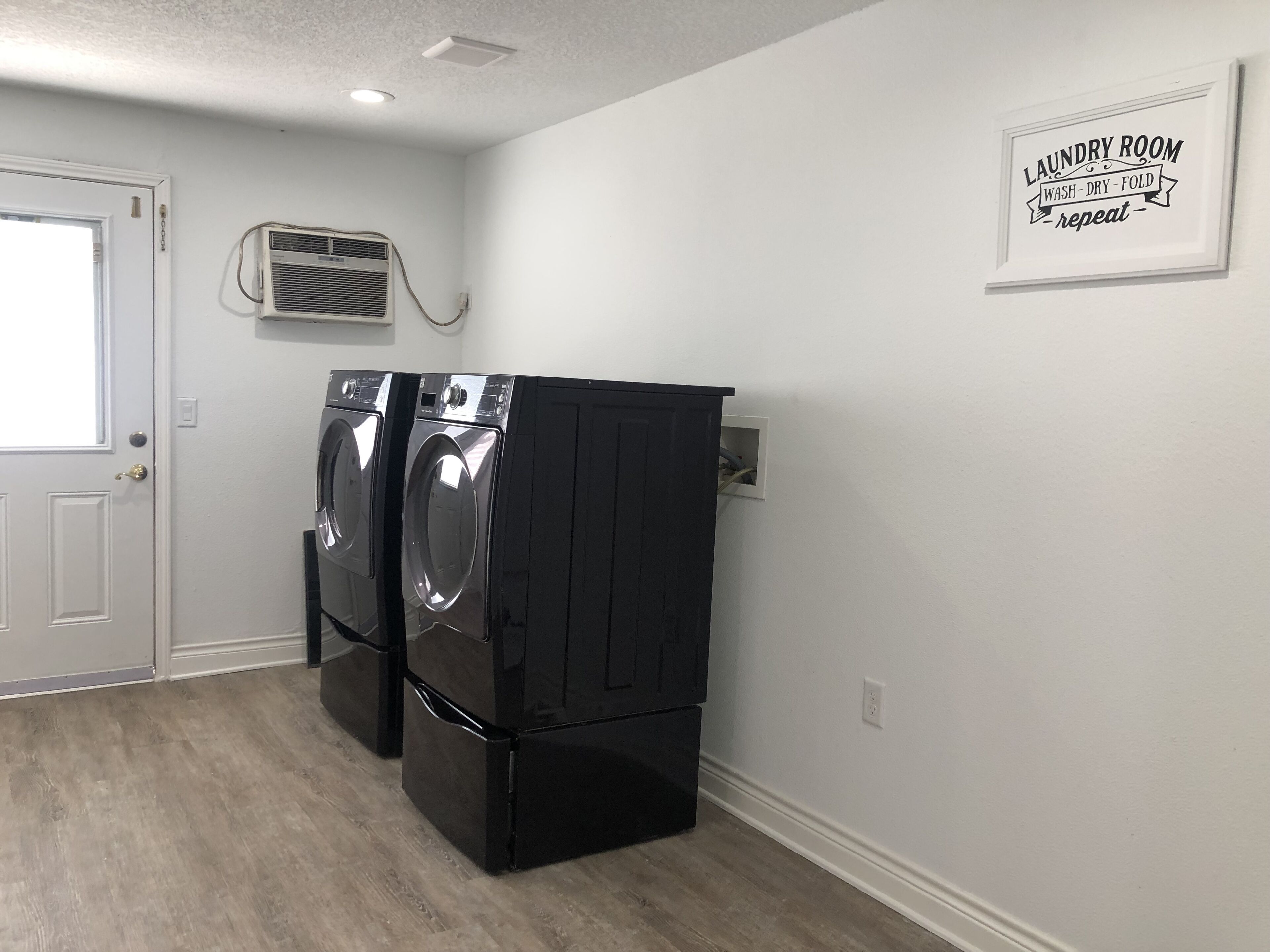 A laundry room with two front-loading washers and dryers, a white door, and a wall-mounted vent.