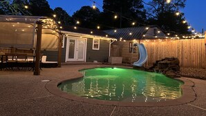 A backyard with a swimming pool, a slide, string lights, and a covered seating area. - Very Nice Country Stay Not Far Away<br> (New Caney)