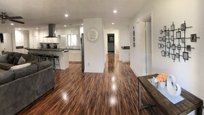 A modern living room with a gray sofa, wooden flooring, a dining area with a dark wooden table, and a kitchen in the background. - Very Nice Country Stay Not Far Away<br> (New Caney)