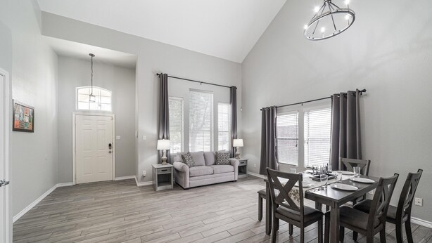 A spacious living room with a dining area, a gray sofa, and a chandelier. - ACL Super Home  . 4 bedroom with Hot spa in the backyard in an awesome neigbohoo (Round Rock)