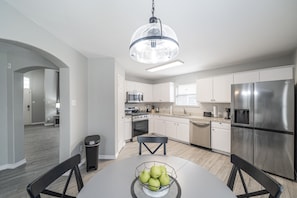 Una cocina moderna con gabinetes blancos, electrodomésticos de acero inoxidable y un comedor con mesa y sillas.