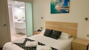 A hotel room with a bed, a nightstand, a wall-mounted painting, and a bathroom visible through an open door.