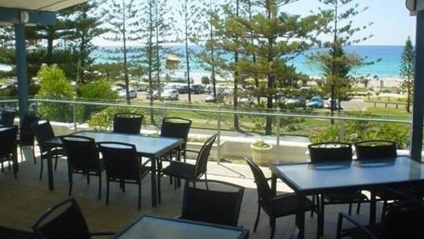 An outdoor patio with tables and chairs, overlooking a beach and ocean.