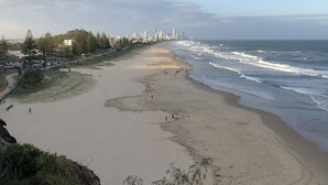 A beach with a city skyline in the distance, sandy shore, and rocky outcrops.
