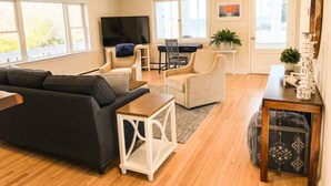 Ein Wohnzimmer mit einer Couch, Sesseln, einem Fernseher, einem Schreibtisch und einer Pflanze.
