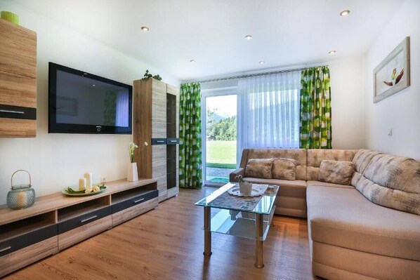 A modern living room with a flat-screen TV, a glass coffee table, a sofa, and a wooden entertainment unit.