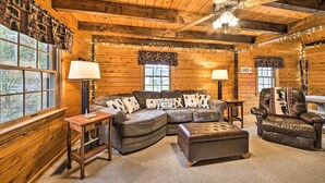 Interior acogedor de una cabaña de madera con un sofá seccional de cuero, un sillón de cuero y una mesita con una lámpara.