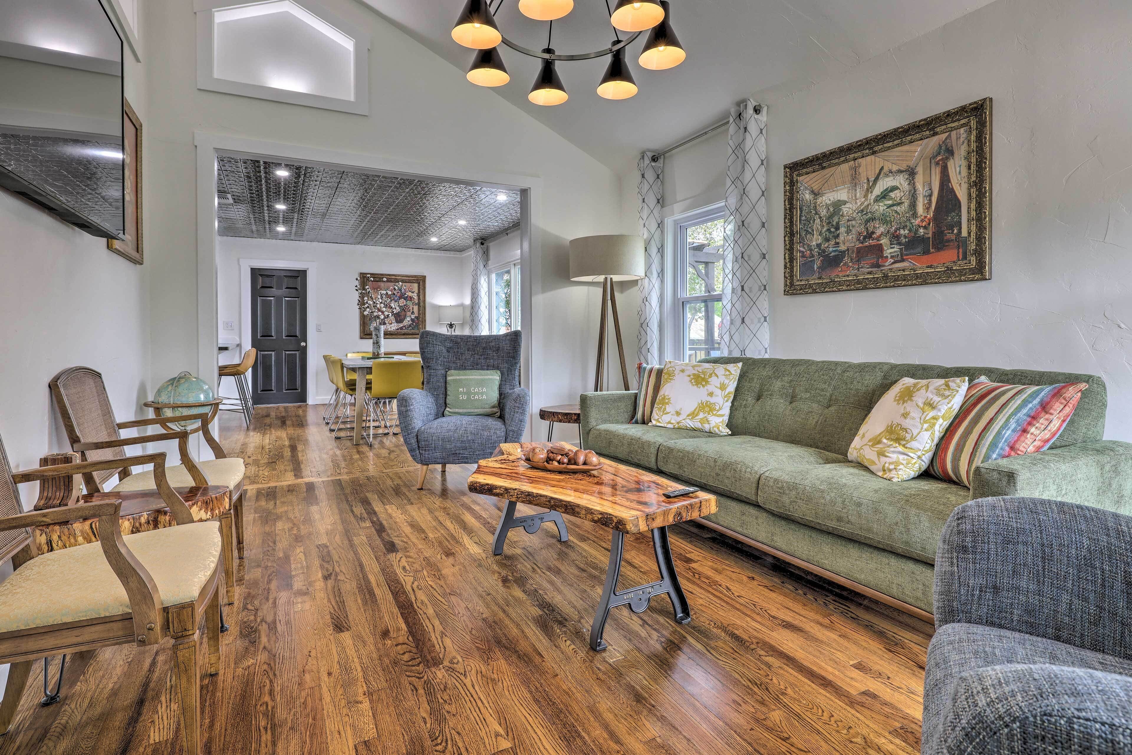 Ein Wohnzimmer mit Couchtisch aus Holz, grünem Sofa und Holzstühlen.
