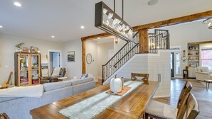 A spacious living area with a wooden dining table, a gray sofa, and a staircase leading to an upper level.