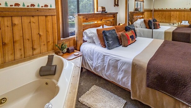 A room with two beds, a wooden wall, a bathtub, and a window with a view of trees. - Romantic Couple's Retreat steps from Village, Kid-Friendly, Fireplace, WiFi (Big Bear Lake)