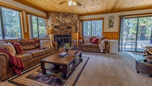 A cozy living room with a stone fireplace, leather sofas, and a large window overlooking a forest. - Romantic Couple's Retreat steps from Village, Kid-Friendly, Fireplace, WiFi (Big Bear Lake)