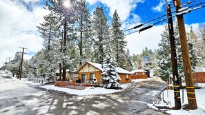 A cabin with a wooden exterior, surrounded by snow-covered trees and a clear sky.