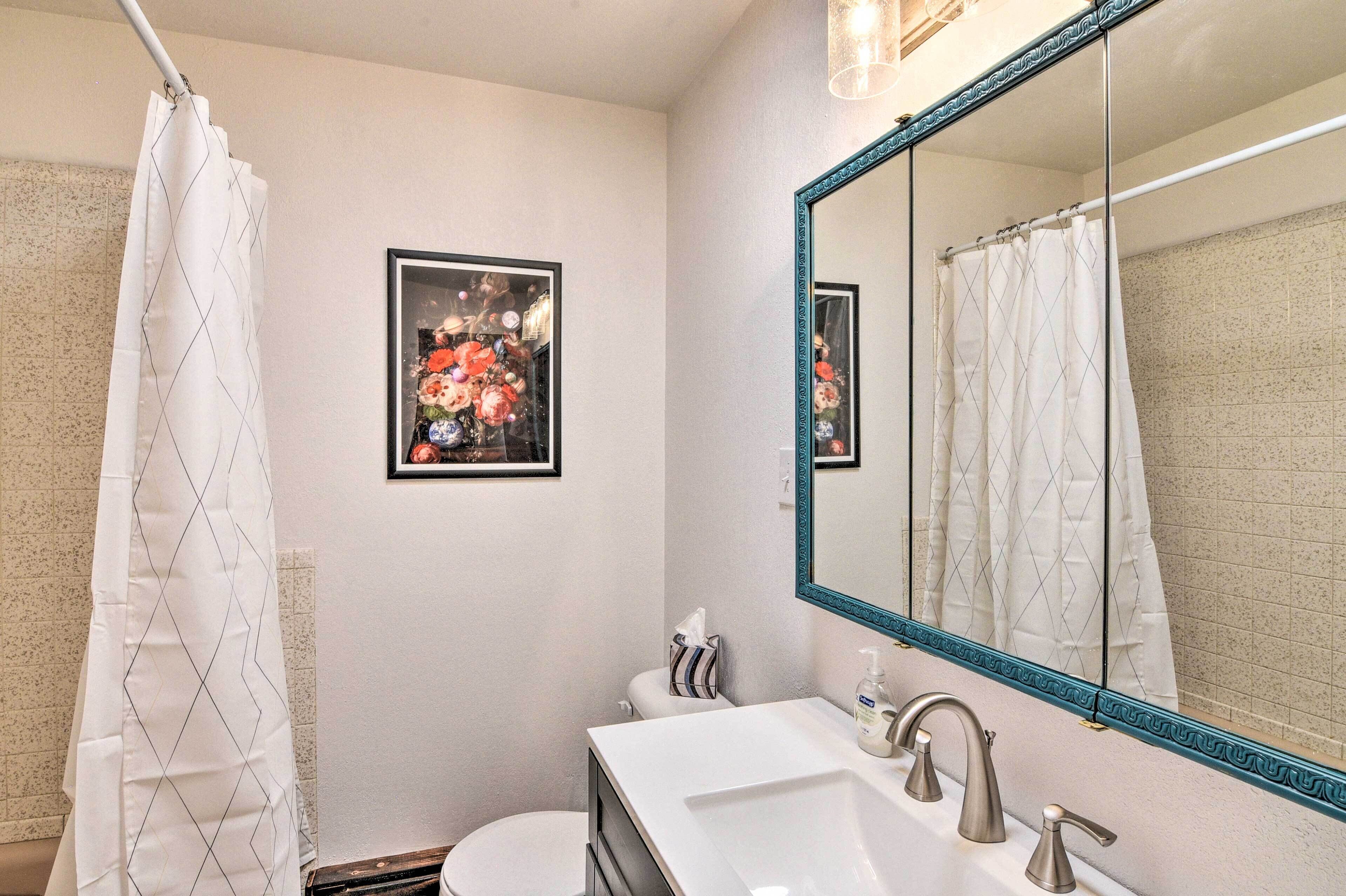 A bathroom with a white sink, a mirror with a decorative frame, a shower curtain, and a framed floral picture on the wall.