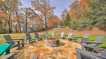 Relax by the fire pit surrounded by Adirondack chairs in a serene wooded setting.