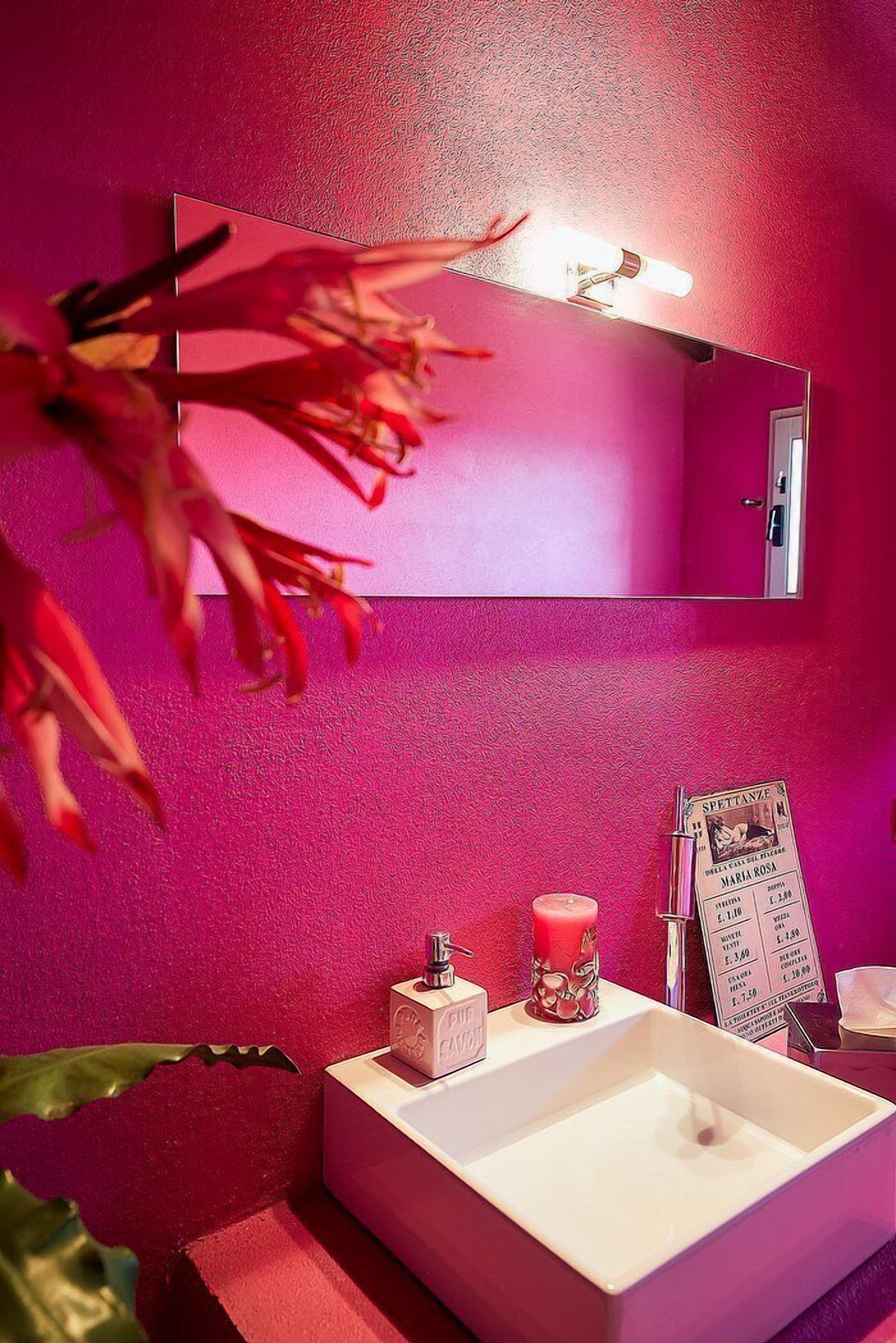 A bathroom with a pink wall, a white sink, a mirror, a candle, and a sign.