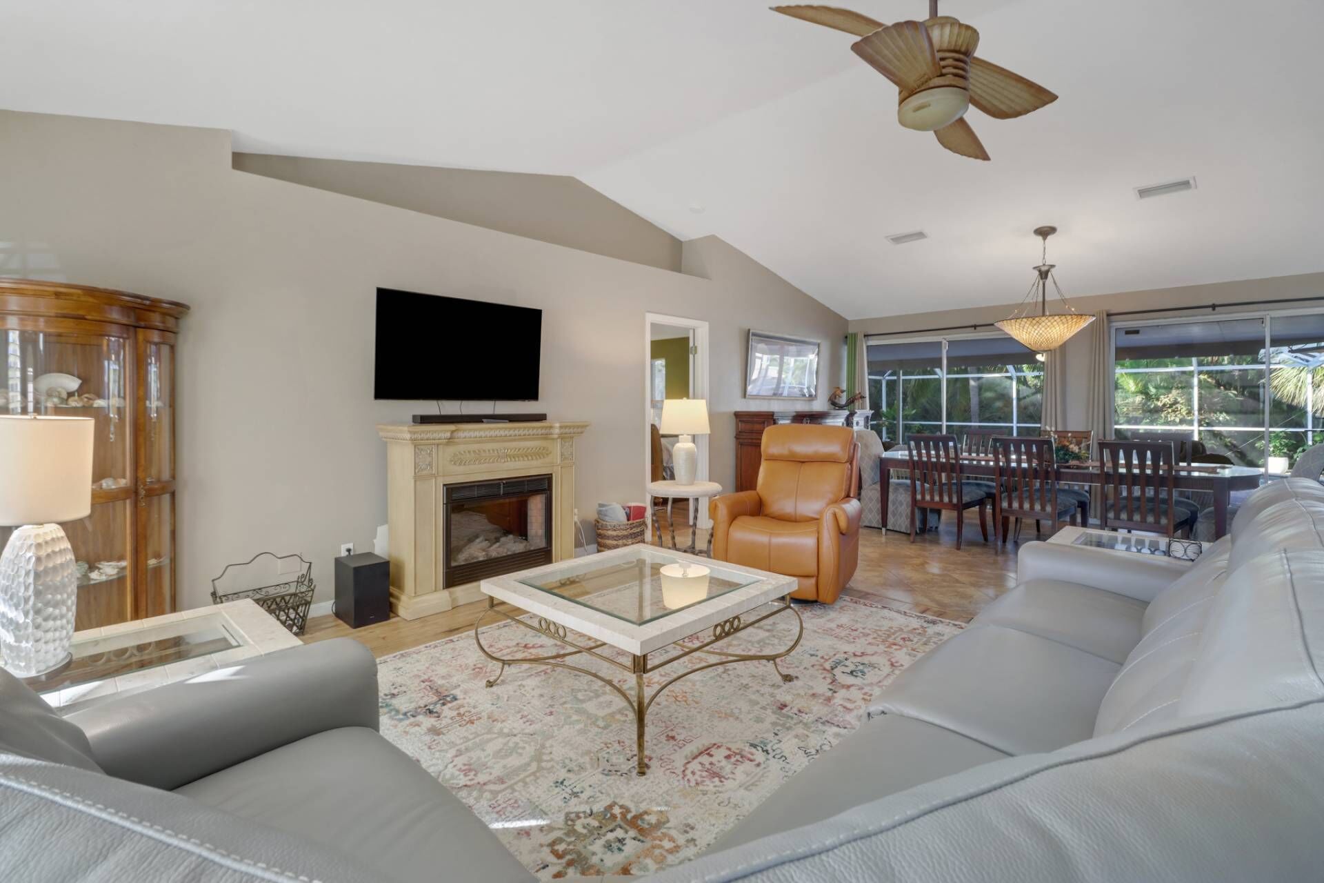 A spacious living room with a fireplace, a television, a large sofa, and a dining area with a view of the outdoors.