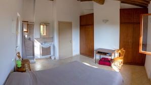 A bedroom with a bed, a desk, a chair, a wardrobe, and a bathroom with a sink and mirror. - Independent Villa l'Aia in a panoramic and quiet position on the Gulf of Lacona (Capoliveri)