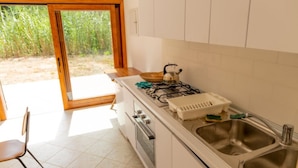 A kitchen with a gas stove, oven, and sink. There is a chair and a sliding glass door leading to an outdoor area. - Independent Villa l'Aia in a panoramic and quiet position on the Gulf of Lacona (Capoliveri)
