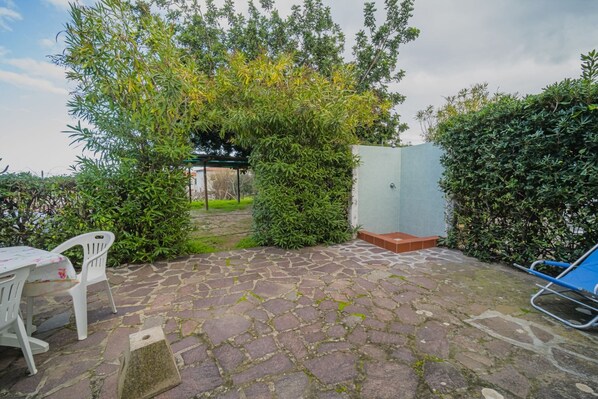 A patio with stone flooring, a covered seating area, and a view of a garden.