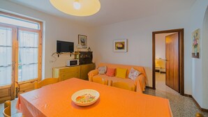 A room with a dining table, a sofa, a television, and a microwave. - APPARTAMENTI SANT'ANDREA - CASA GRANDE ALLE PIANE (Marciana)