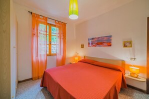 Een slaapkamer met een bed, twee bedlampen, een raam met gordijnen en een schilderij aan de muur.