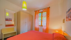 A bedroom with a bed, a wardrobe, a mirror, and a window with curtains. - APPARTAMENTI SANT'ANDREA - CASA GRANDE ALLE PIANE (Marciana)