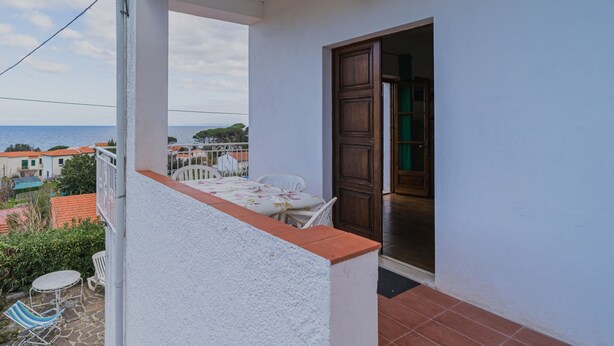 Ein Balkon mit Tisch und Stühlen, Blick auf das Meer und eine Holztür.