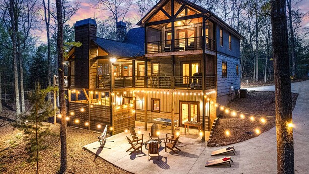 A two-story log cabin with a balcony, surrounded by trees and string lights.