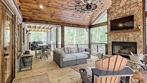 A covered outdoor living area with a stone fireplace, a ceiling fan, and a seating area with a sofa and chairs.