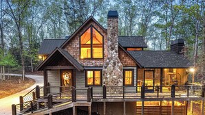 A log cabin with a stone chimney, large windows, and a deck.
