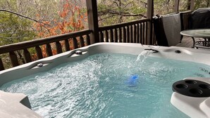 Un bain à remous avec de l’eau en mouvement, entouré d’une terrasse en bois et offrant une vue sur les arbres aux couleurs automnales.