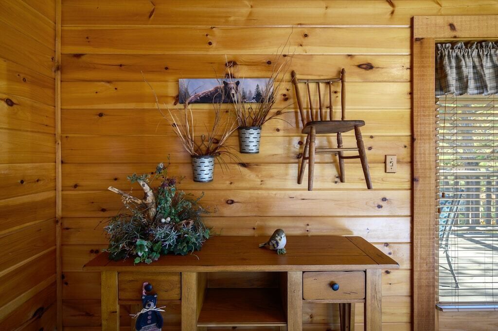 A wooden cabin interior with a wooden desk, two chairs, and decorative plants.
