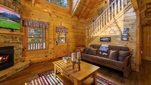 L’intérieur d’un chalet confortable, avec des murs en rondins de bois, une cheminée en pierre, une table en bois, un canapé et un escalier.