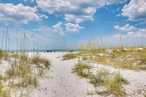 Ein sandiger Pfad am Strand, der zum Meer führt, mit spärlicher Vegetation.
