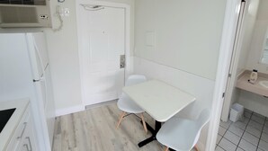 Una cocina pequeña y moderna con una mesa y sillas blancas, un refrigerador blanco y un aire acondicionado instalado en la pared.