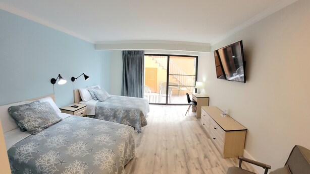 Habitación de hotel con dos camas, un escritorio, una silla, un televisor y un balcón con vistas.