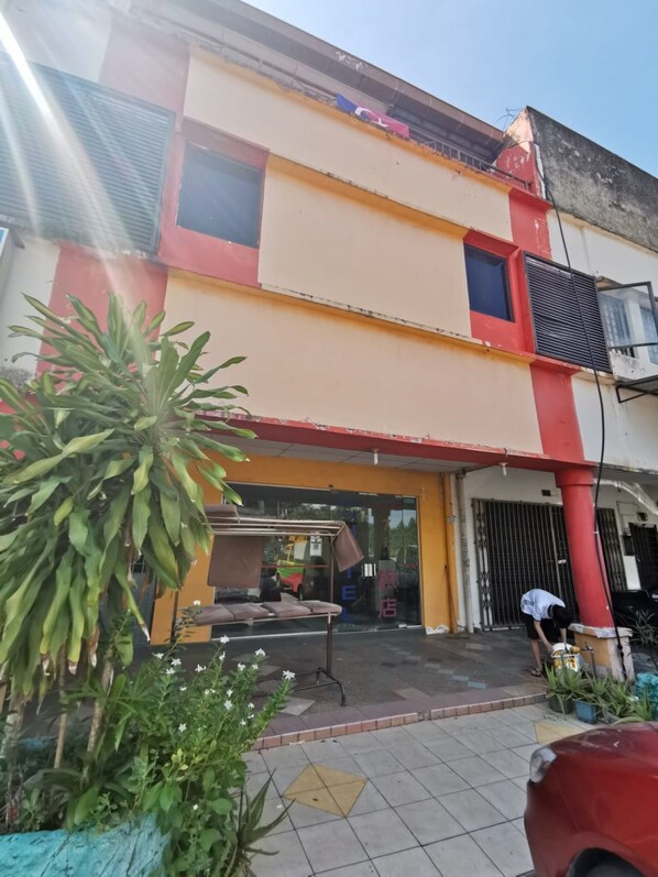 Un edificio de dos pisos con fachada roja y amarilla, una entrada con portón y una persona trabajando cerca de la entrada.