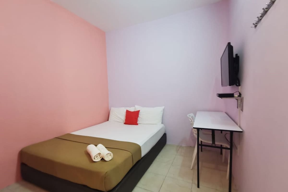 Habitació petita amb un llit individual, una taula i una cadira, un televisor fixat a la paret i un parell de tovalloles arremolinades al llit.
