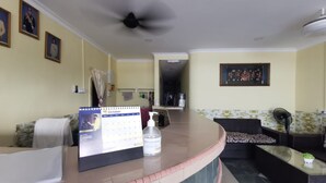 A hotel lobby with a reception desk, a calendar, a hand sanitizer dispenser, a sofa, a coffee table, and a ceiling fan. - Hotel O My Seven Days Inn (Masai)