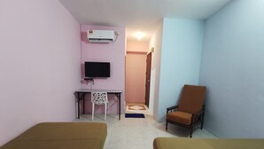 A hotel room with two beds, a desk with a chair, a television, and an air conditioning unit.