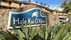 Letrero de Hale Kai O'Kihei con un símbolo de tortuga, rodeado de plantas tropicales y palmeras.
