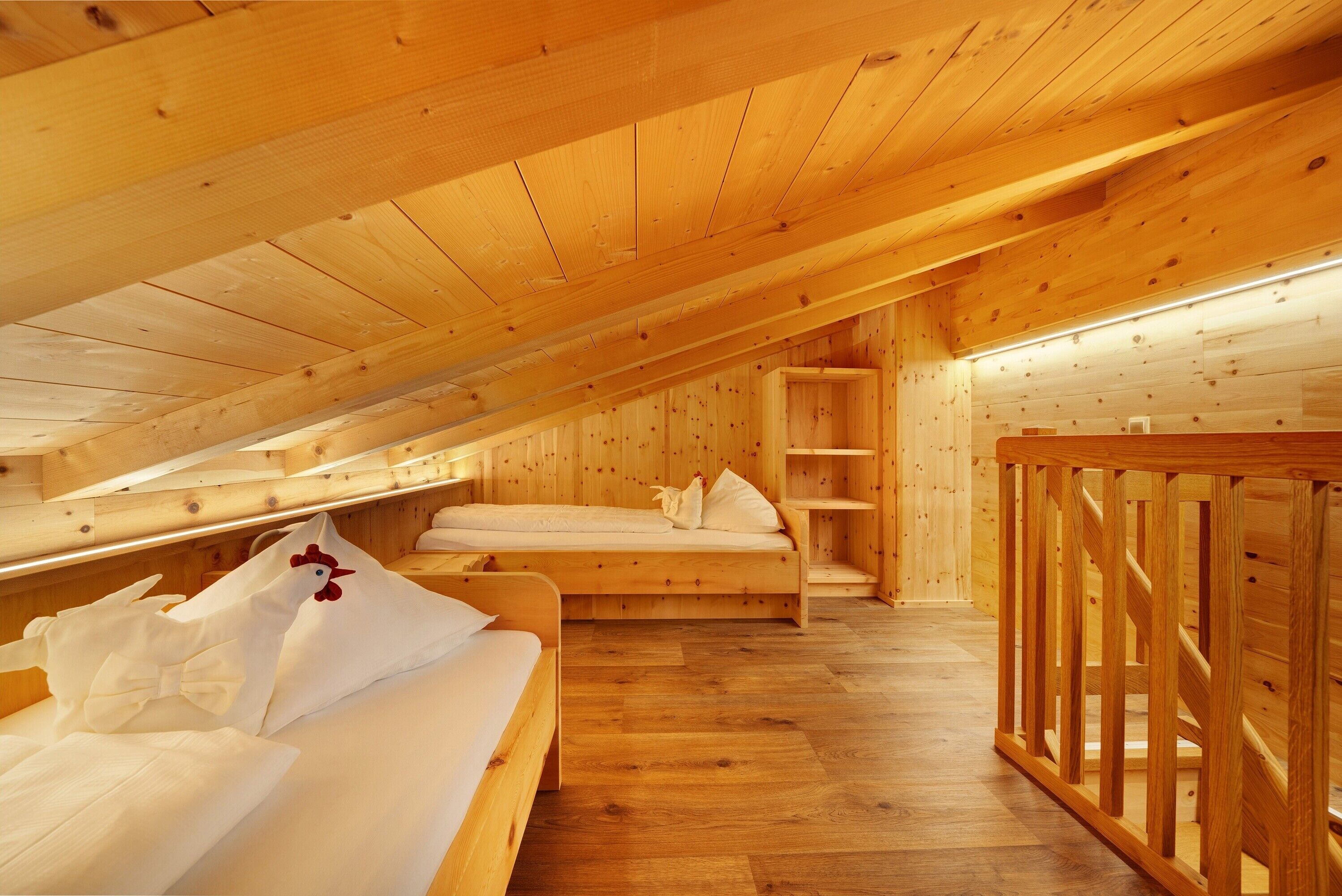 Interior de madera con techo inclinado, una cama con ropa de cama blanca y una barandilla de madera.