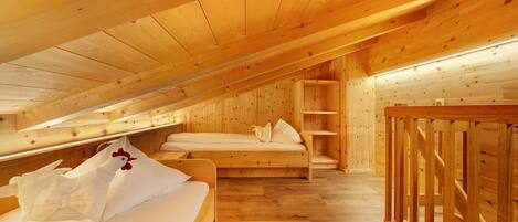 Interior de madera con techo inclinado, una cama con ropa de cama blanca y una barandilla de madera.
