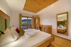 A bedroom with a wooden ceiling, a bed with pillows, a wooden desk, a mirror, and a view of the outdoors. - Thalerhof Apartment Katrin with Wi-Fi, Balcony & Garden (Vöran)