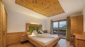 Ein Schlafzimmer aus Holz mit Bett, Nachttischen, Schreibtisch und einem Balkon mit Blick.