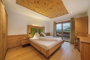 Un dormitorio de madera con cama, mesitas de noche, un escritorio y un balcón con vistas.