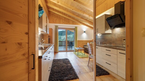 Een houten interieur met een keuken, een eethoek en uitzicht door een glazen deur.